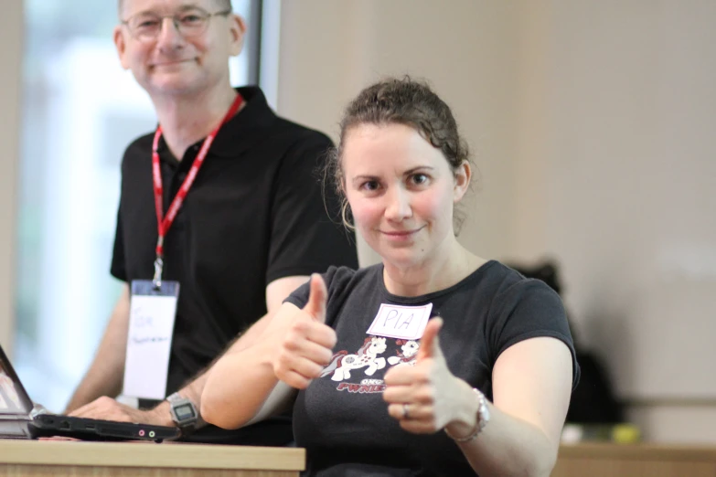 a woman giving a thumbs up with a computer behind her