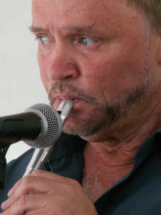 a man with a pen in his mouth speaking into a microphone