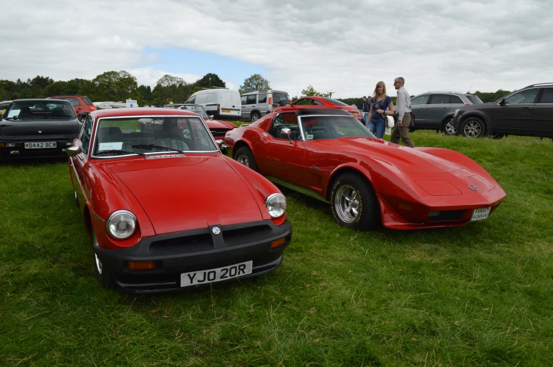 red sports cars parked in a field while people look on