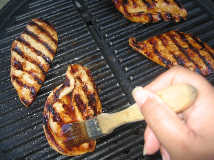 a person using a brush on some bbq chicken