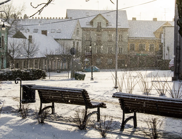 two empty park benches covered in snow at city park