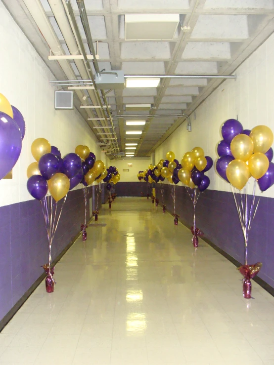 purple and gold balloons with gold streamers on them are standing in a long hallway