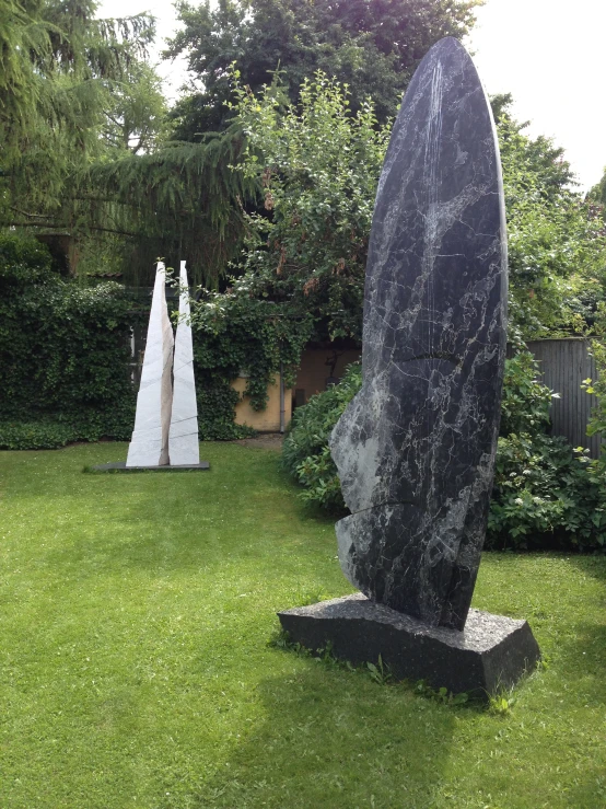 two stone sculptures in the grass outside near trees