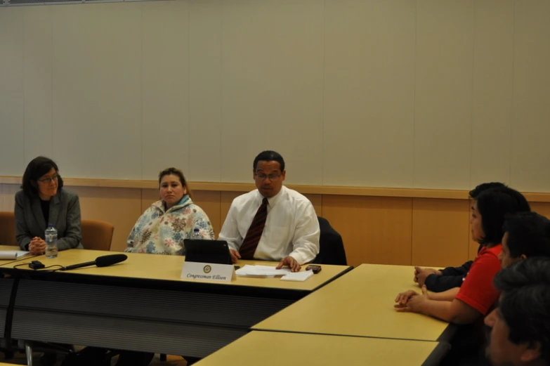 three people sitting at a table, two of them looking at a laptop