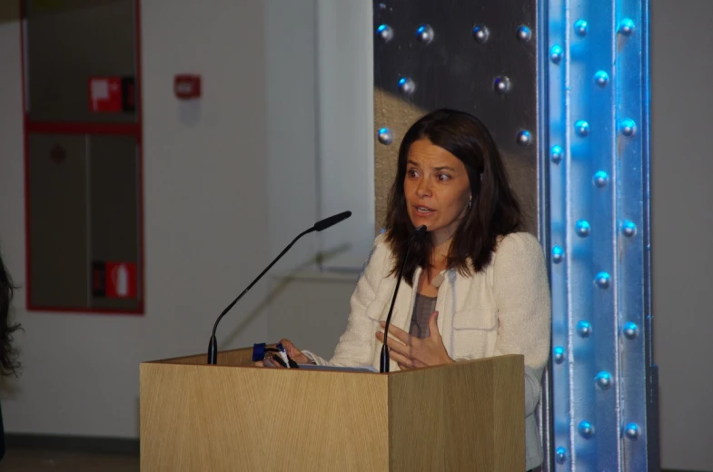 a woman standing at a podium holding a book and looking off into the distance