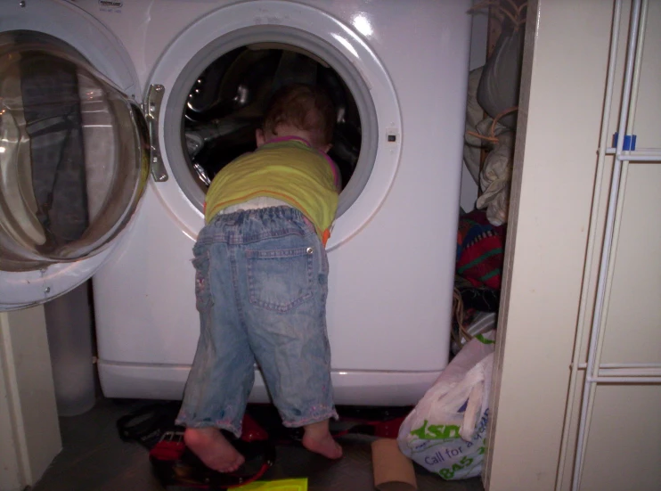 a boy in a yellow shirt standing on the front of a washing machine