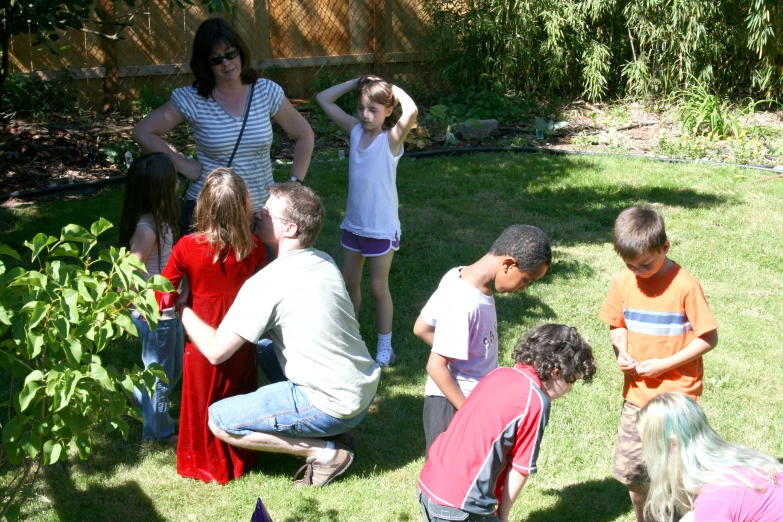 a group of children in front of a woman in a backyard with the child on the grass