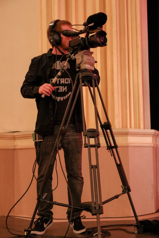 man looking up at camera, standing by tripod with headphones on
