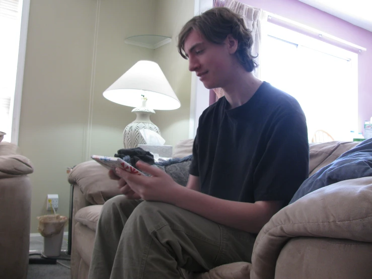 a young man is sitting on a couch while playing with his phone