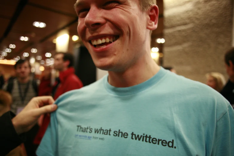 a man smiles while holding a t - shirt with words on it
