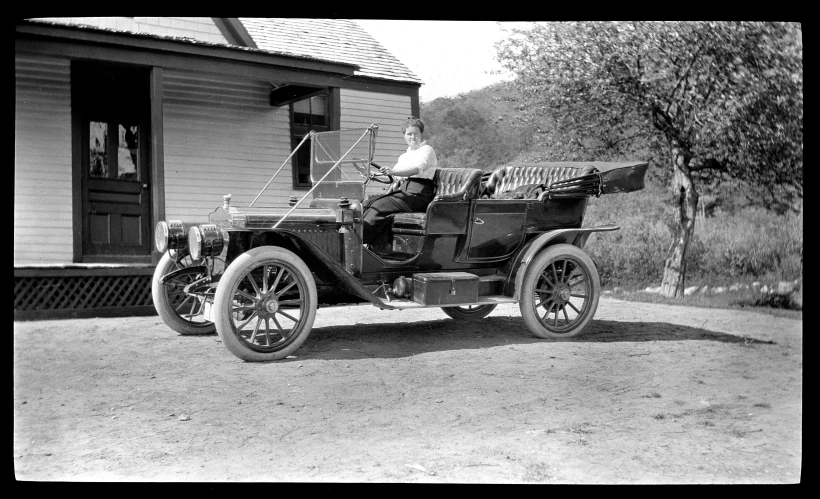 an old time black and white po shows a man sitting on an older looking car