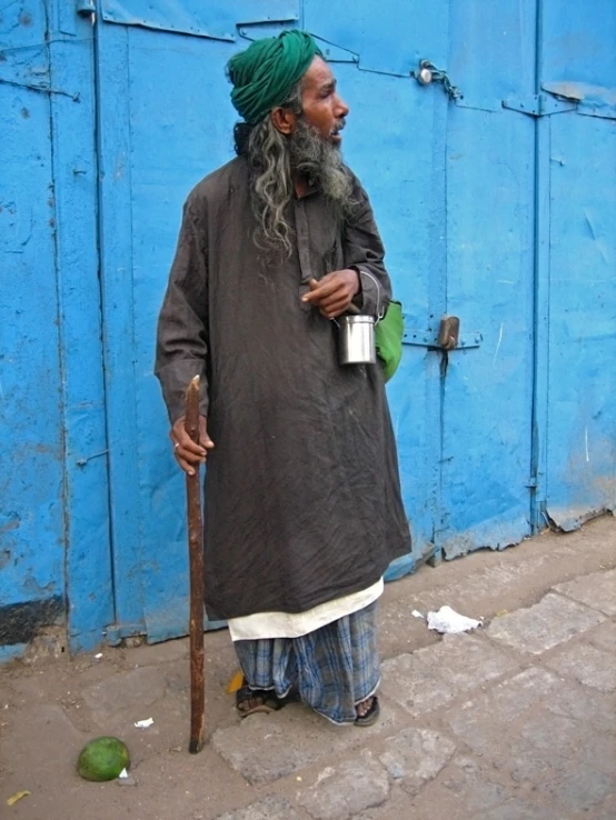 an old man standing on the sidewalk holding his cup and looking off to the left