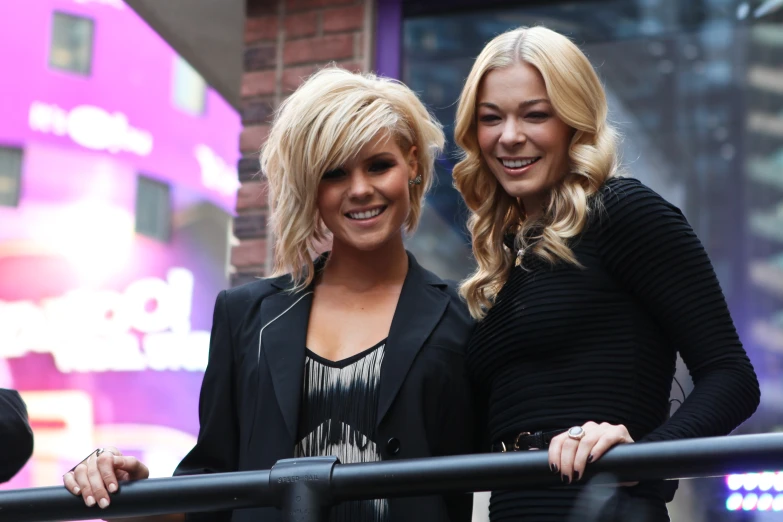 two blond woman posing for the camera in front of a building