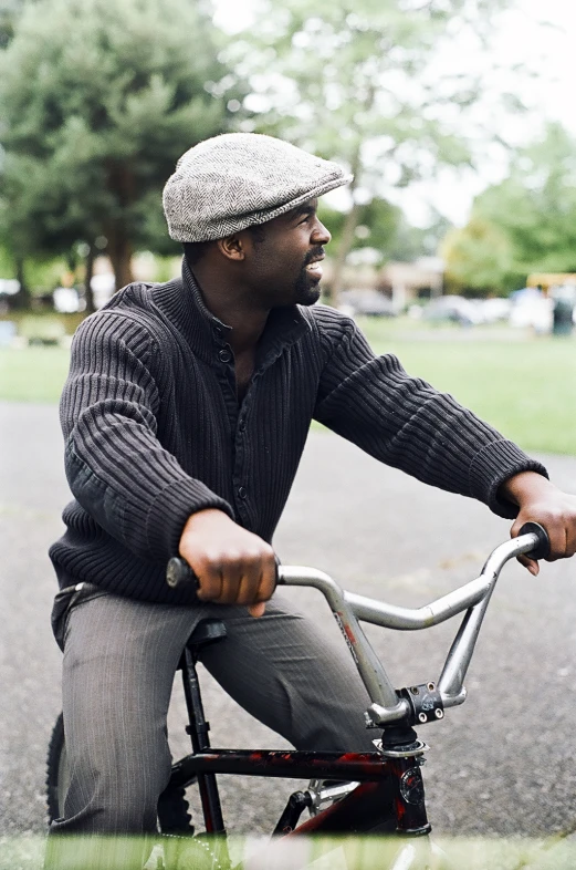 a man in a hat and cardigan riding a bicycle
