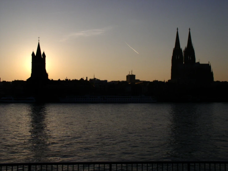 the sun setting behind an ancient cathedral overlooking a body of water