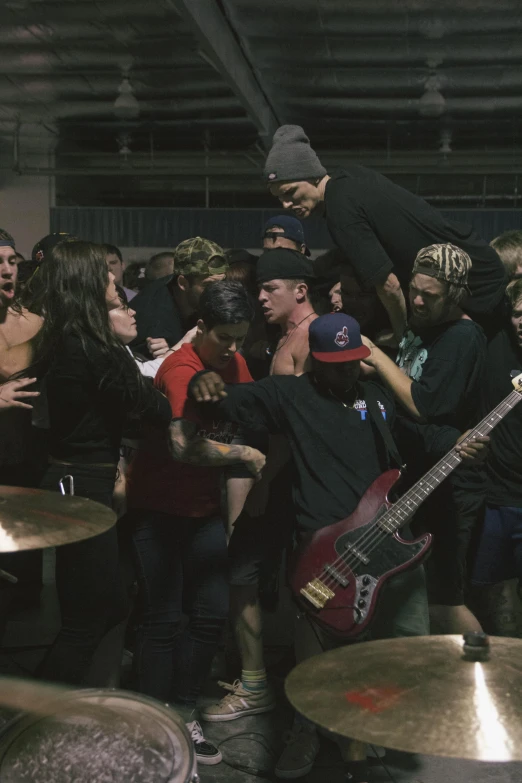 man balancing a guitar while people crowd in background