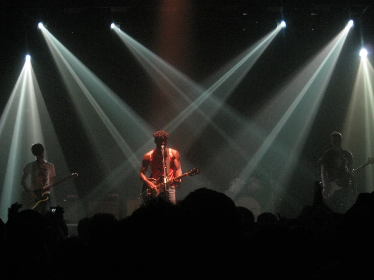 two men and a woman standing on stage with guitars