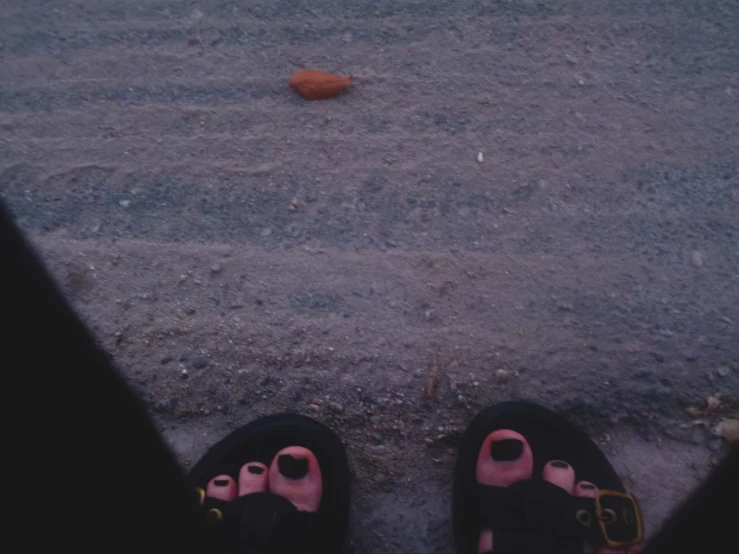 legs in sandals and a orange peel sitting in the sand