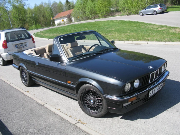 an old bmw is parked next to a car on the side of the road