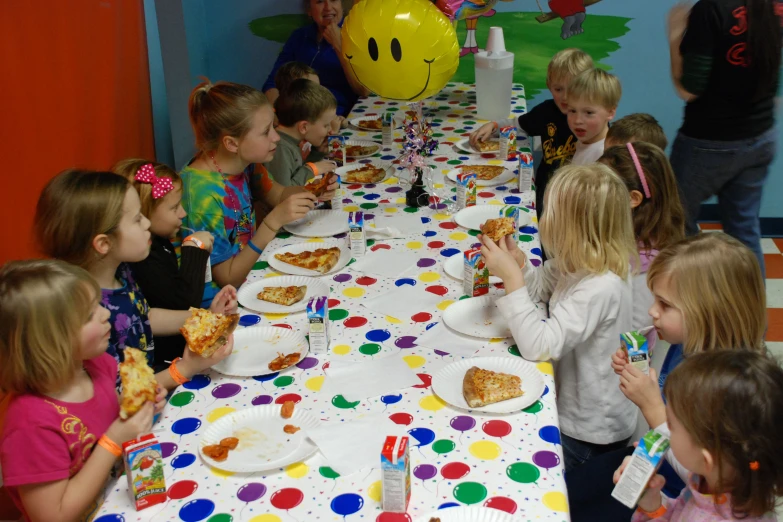 a large group of children sitting at a table eating pizza