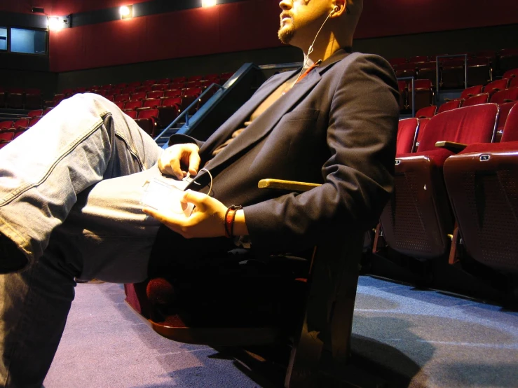 a man in a blazer sits on the bench of a theater