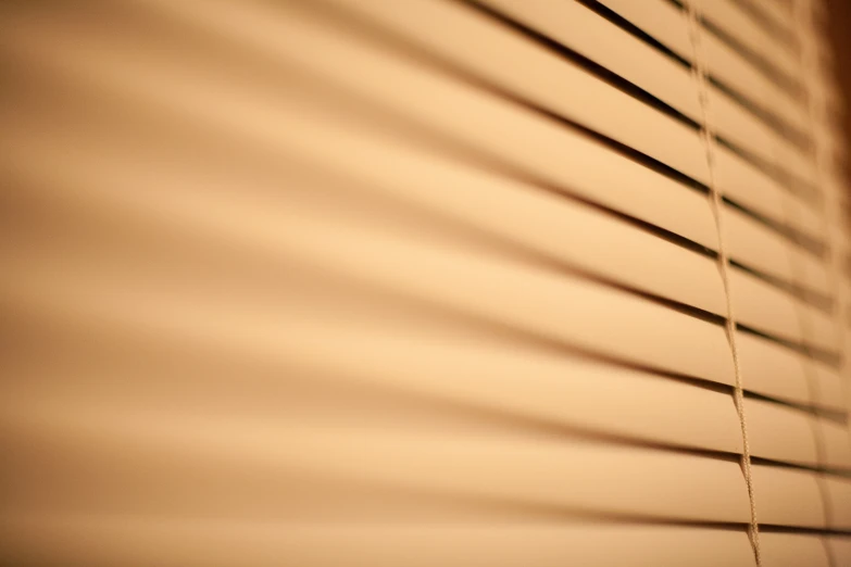 a closeup s of some tan blinds with the shadow cast by it