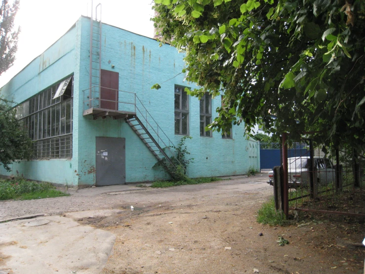 a blue building on the side of a dirt road with trees surrounding it