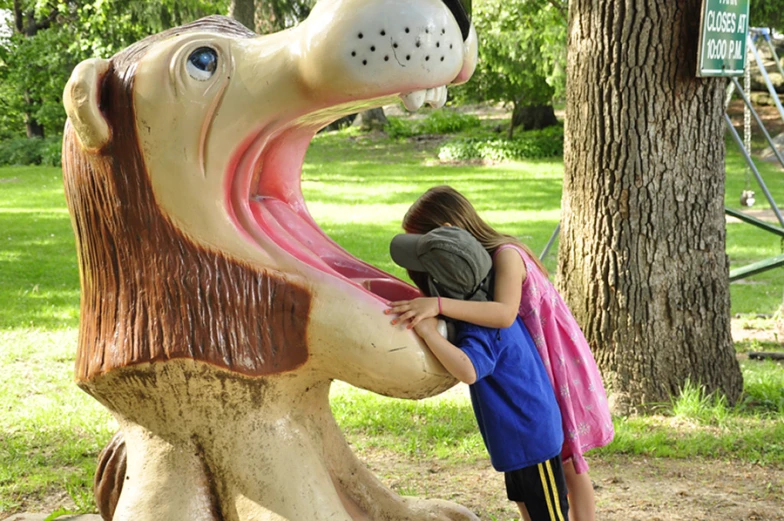 girl and boy on animal statue with playground in the background