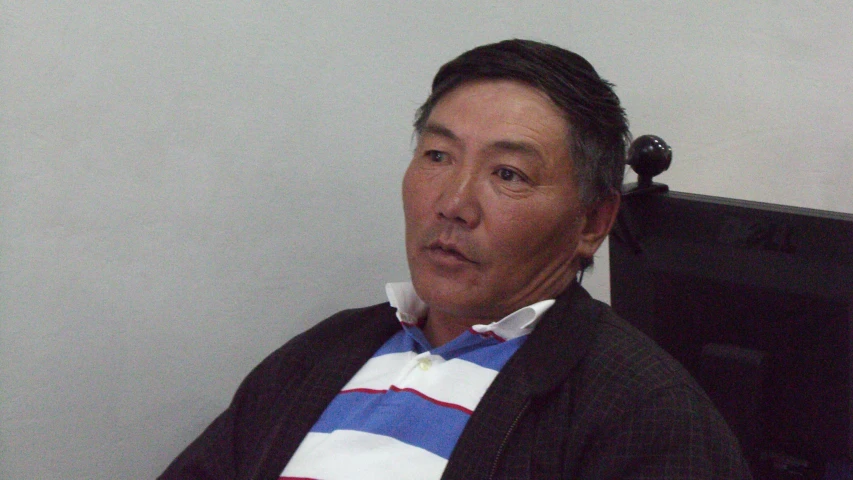 an asian man wearing a sweater and tie sitting down