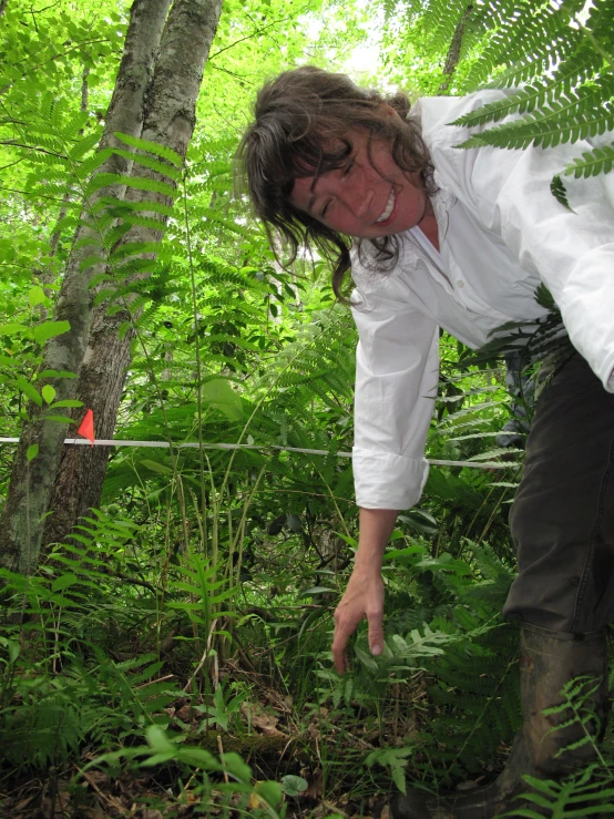 a man bending down in a forest surrounded by ferns