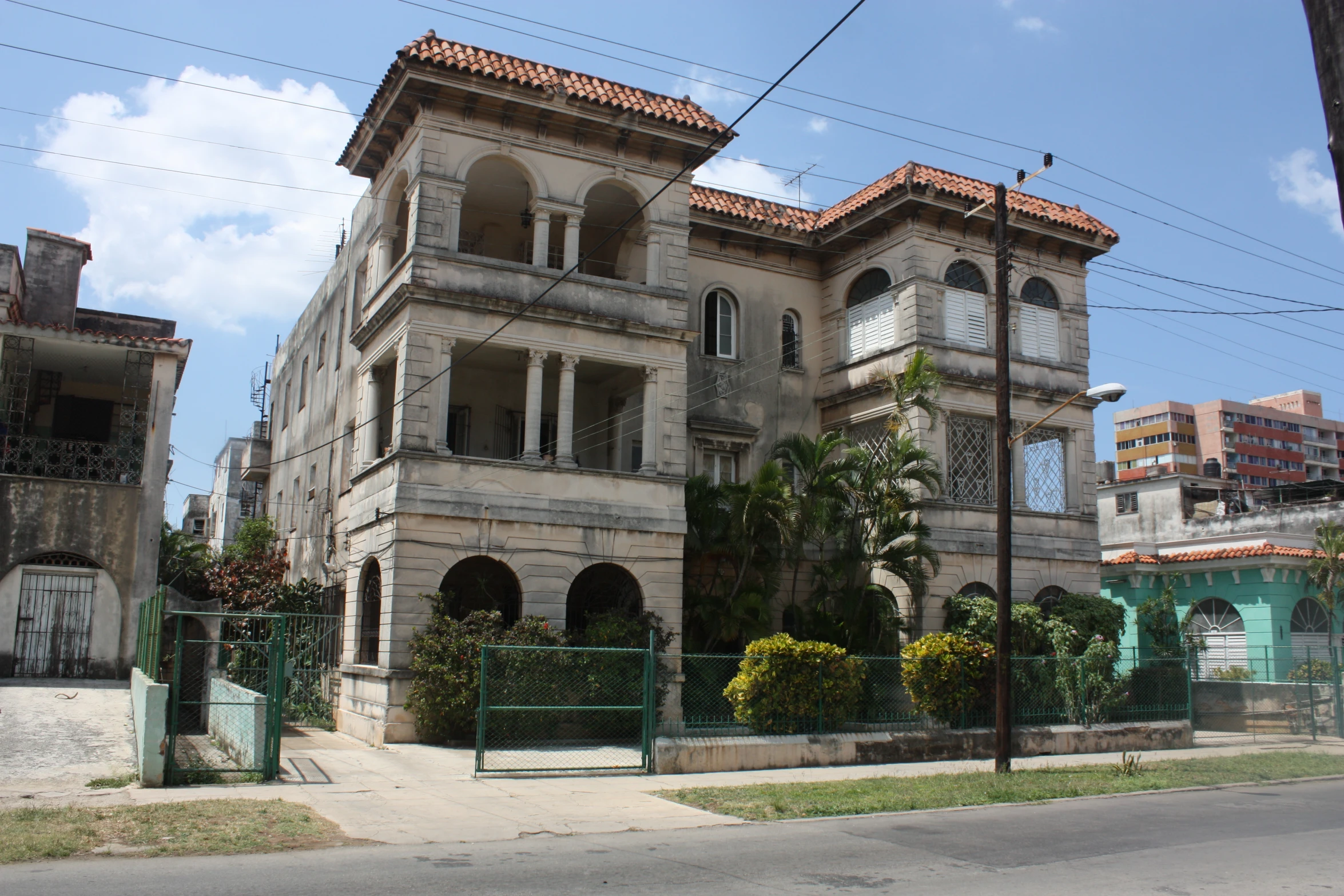 old, stone colored building stands next to a green fence