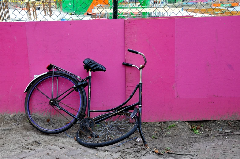 a bike leaning against a pink wall in front of a graffiti - covered wall