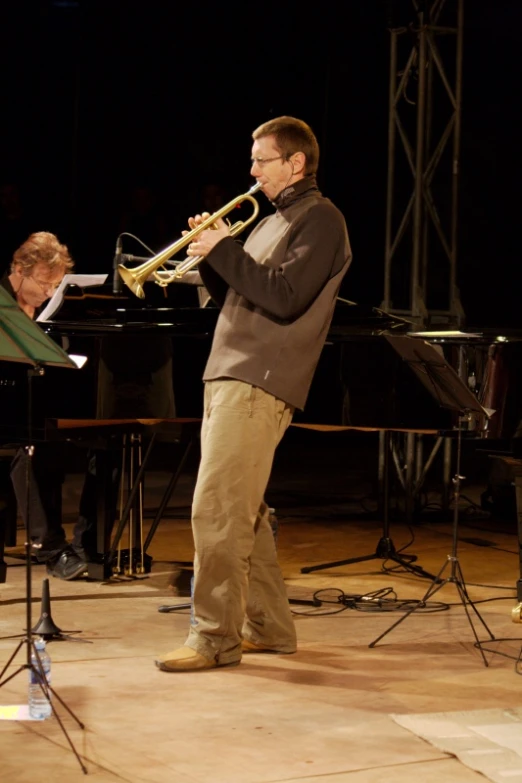 a man with glasses and a black jacket playing a trumpet