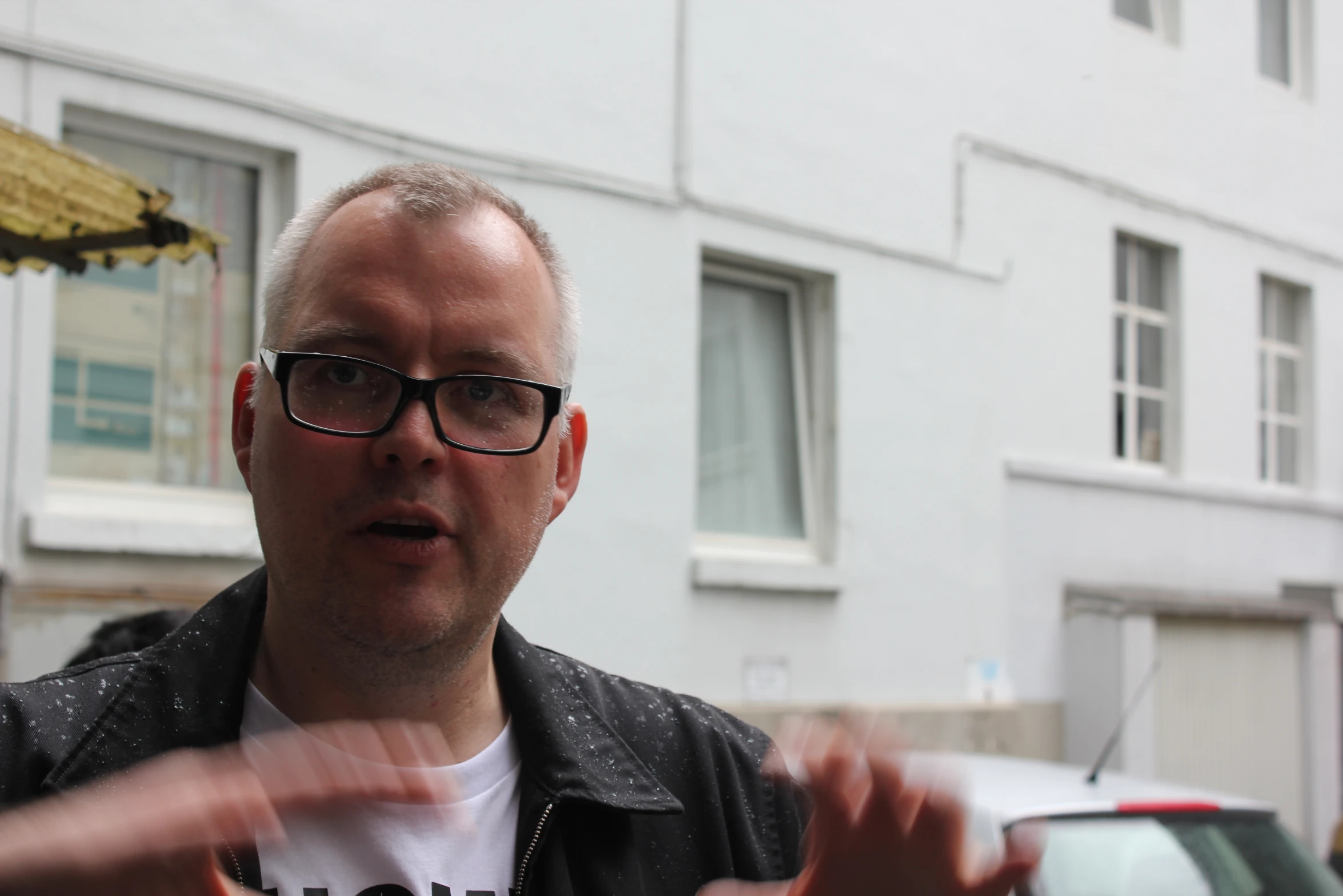 a man wearing glasses talking while standing outside