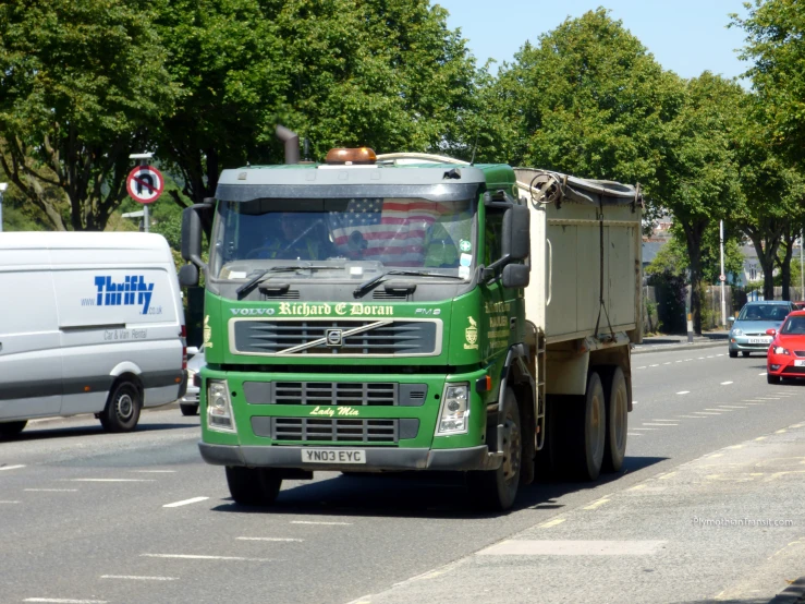 green dump truck driving down the road surrounded by traffic