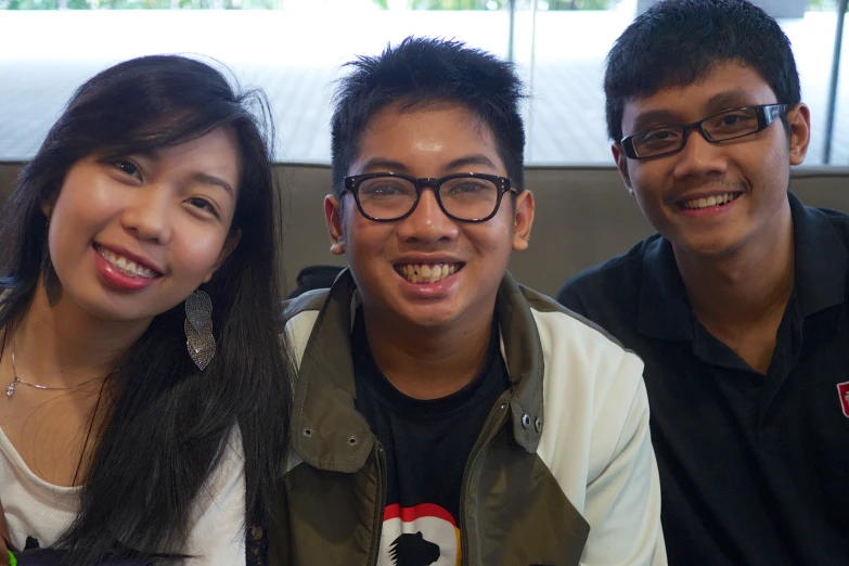 three people smile at the camera with one holding a cellphone