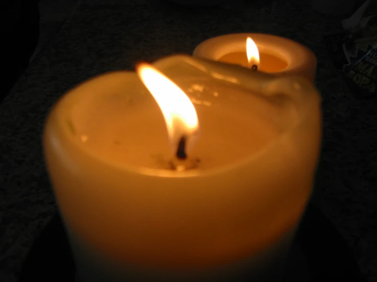 two yellow candles with one lit with a lit light