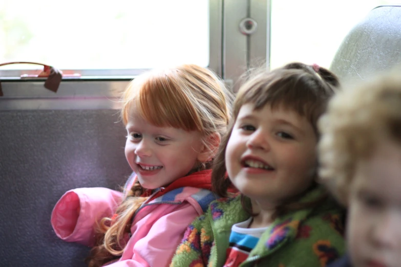 three little girls riding on a bus and smiling