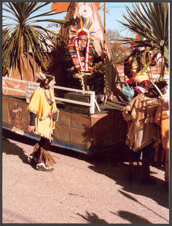 people dressed in native garb walk past a float