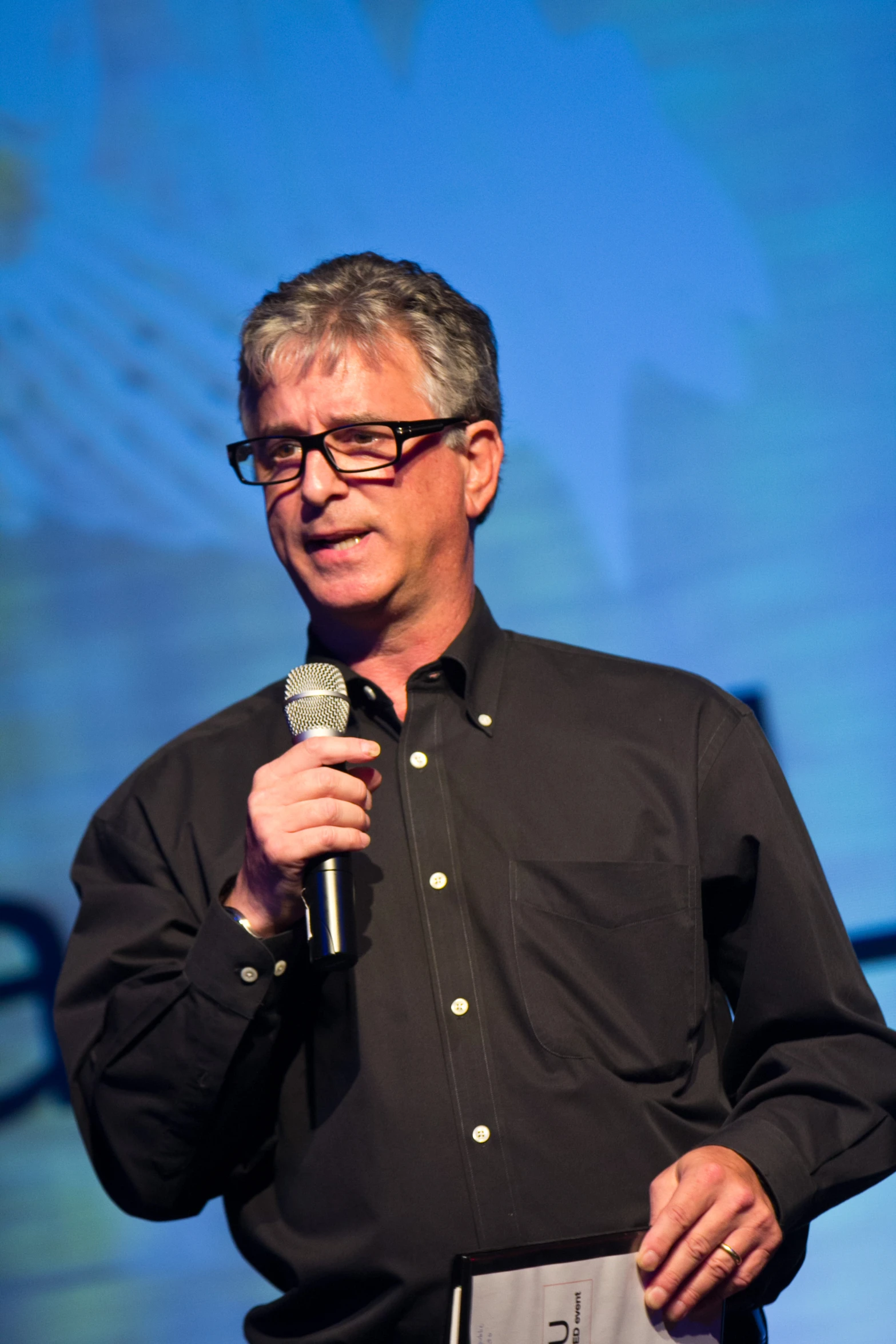 a man speaking into a microphone in front of a blue backdrop