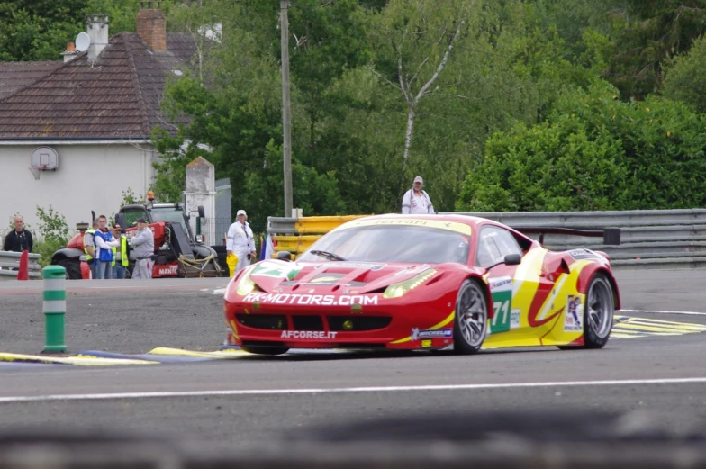 a red and yellow sports car driving on a road near a crowd