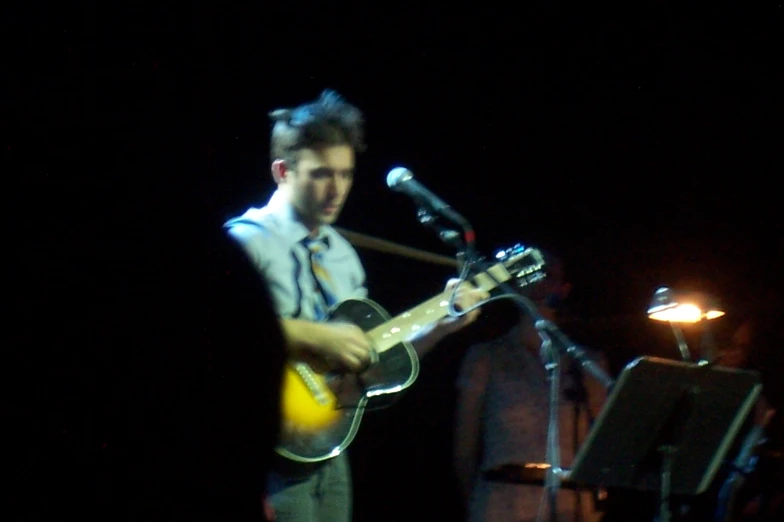 a man with a guitar and microphone in the dark