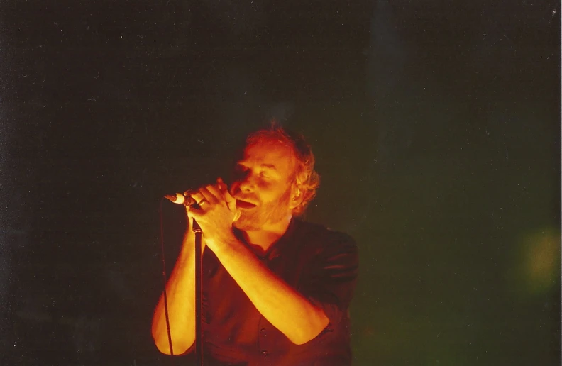 man in red shirt on stage singing into microphone