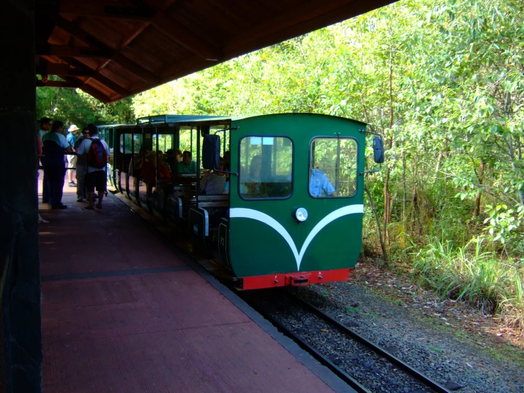 a green train pulling up to the station