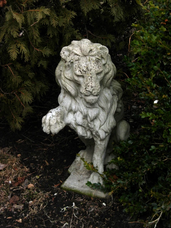 a statue of a crouching white lion in front of trees