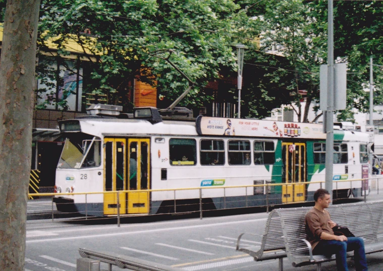 man sitting on a bench next to a public bus