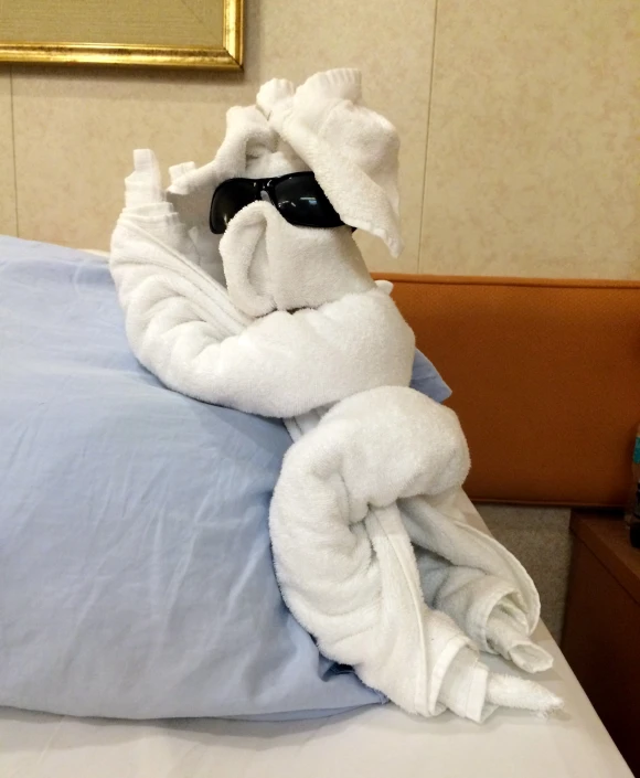 towel animals sitting on the bed together with sunglasses on