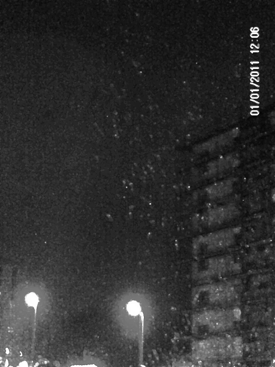 a black and white image of a street at night with several people walking and some of the lights glowing on