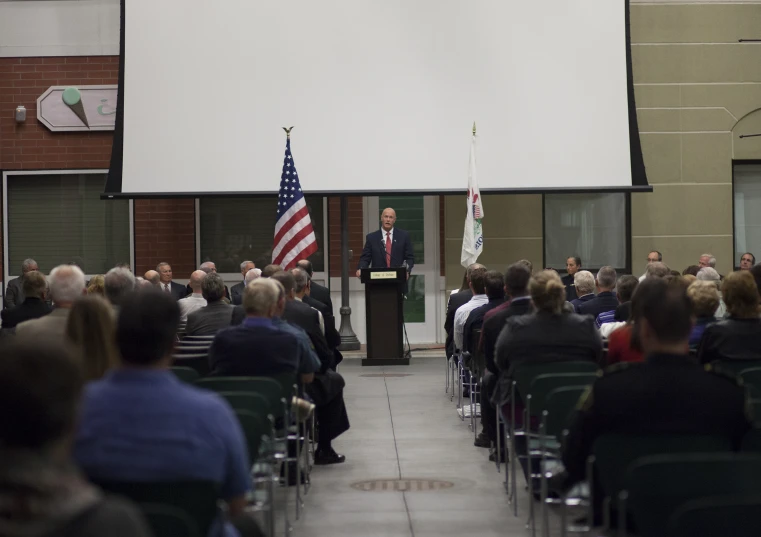 people seated in chairs listening to a man who gives a speech