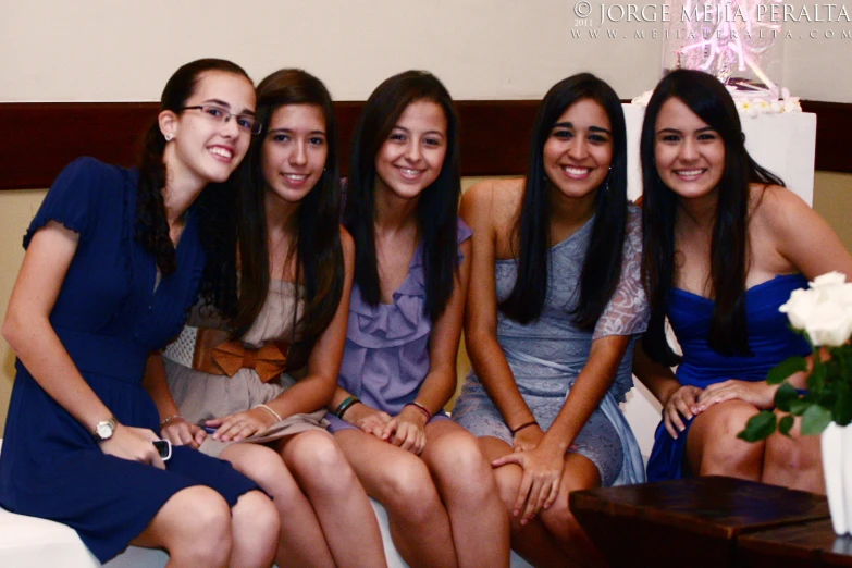 four women sitting next to each other near a flower